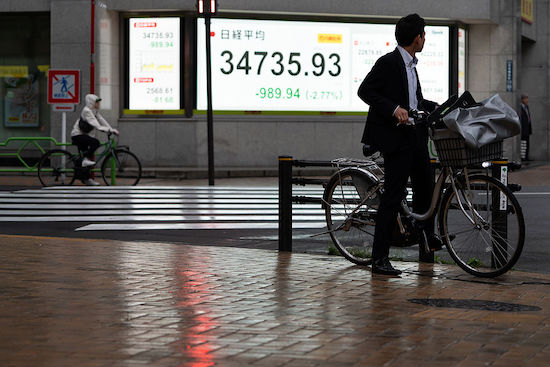 A pedestrian riding a bike looks at an electronic board displaying the Nikkei 225 Stock Average on 3 April 2025 in Tokyo, Japan